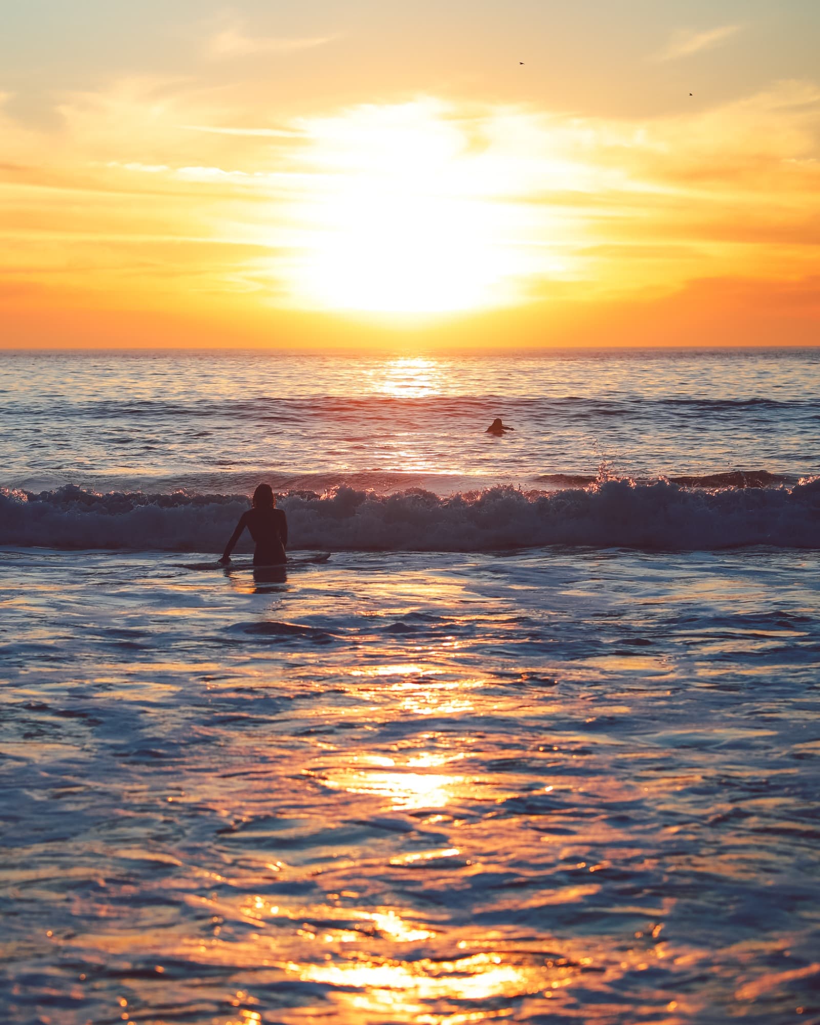 Sunset over ocean waves with a surfer in the foreground